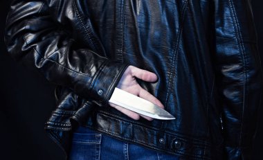 A man in a leather jacket holds a knife behind his back, a black background clipart