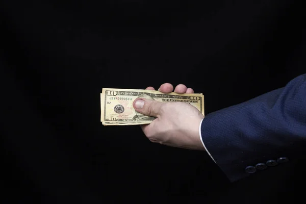 La mano de un hombre con traje sostiene dólares sobre un fondo negro — Foto de Stock