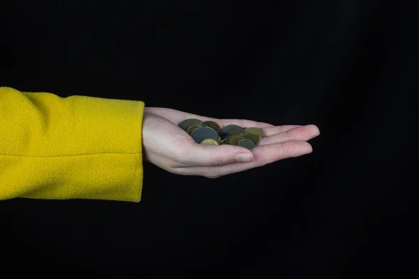 Mano femenina en una chaqueta amarilla sostiene un puñado de monedas, un fondo negro — Foto de Stock