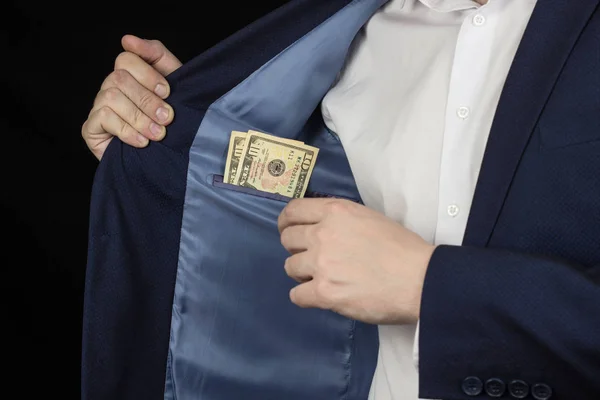 Un hombre en una chaqueta en un bolsillo del pecho sostiene dólares, un fondo negro — Foto de Stock