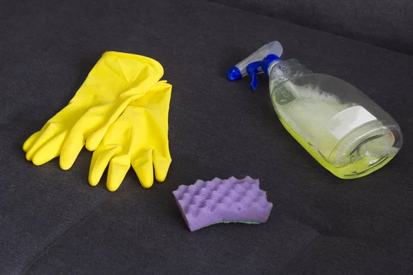 yellow cleaning gloves, a sponge and a cleanser on the couch