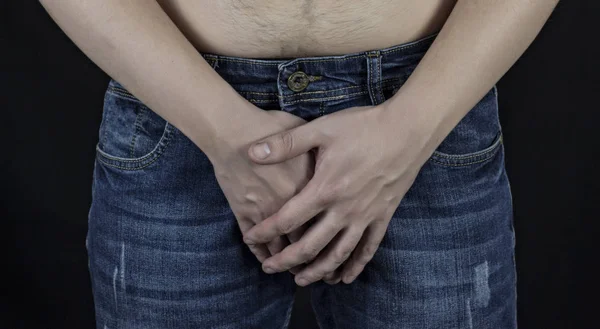 Człowiek w dżinsy trzyma ręce w pachwinie, czarne tło — Zdjęcie stockowe