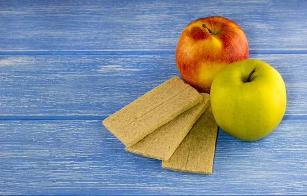 Красное и зеленое яблоко, хлеб на синем деревянном фоне — стоковое фото
