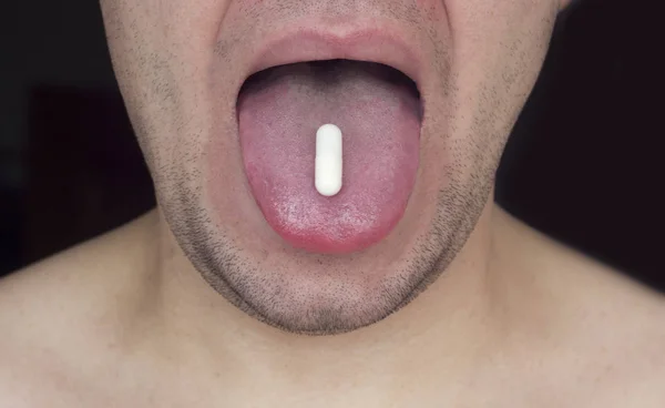 刮胡子的人拿着一块药片在他的舌头, 黑色背景, 特写 — 图库照片