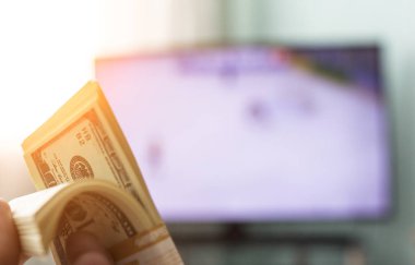 Men's hands hold a bundle of money dollars against the background of a TV on which they show hockey, close-ups clipart