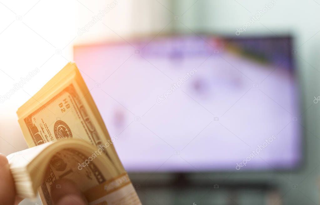 Men's hands hold a bundle of money dollars against the background of a TV on which they show hockey, close-ups