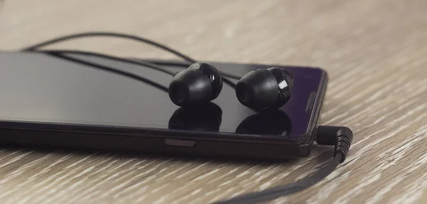 Telefon s černými sluchátka na dřevěné pozadí — Stock fotografie