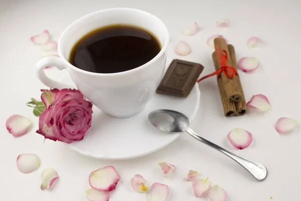 Coffee with cinnamon sticks, rose, chocolate slice on a white background, rose petals