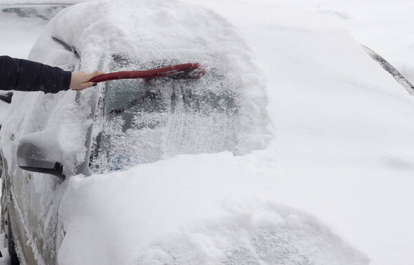 The girl brushes the car from the snow with a brush