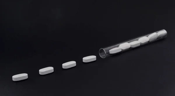 Comprimidos em um tubo de ensaio em um fundo preto — Fotografia de Stock