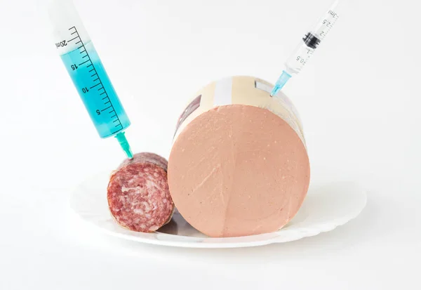 Sausage on a white background in which a syringe is injected with antibiotic and preservatives, close-up, snag hormone