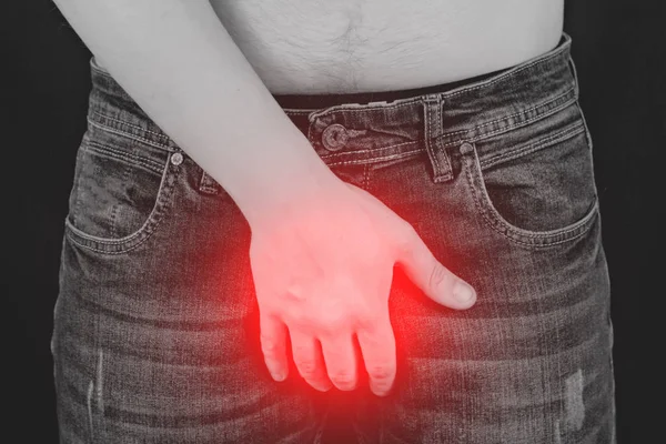 Um homem de jeans está segurando as mãos na virilha, um fundo preto, preto Branco — Fotografia de Stock