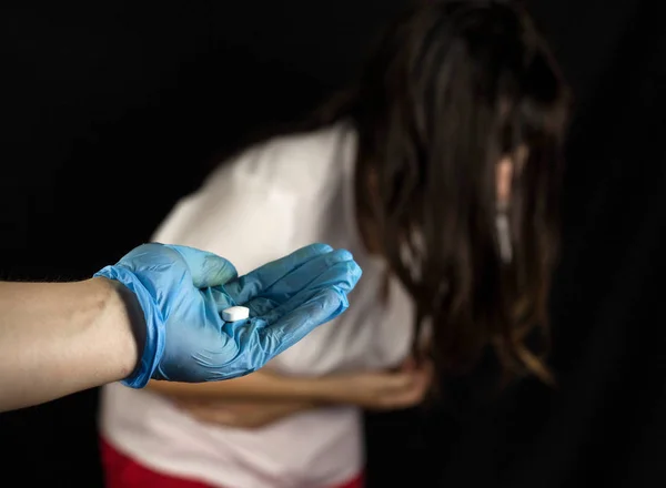 Egy orvos, egy orvosi kesztyűben tart ki egy pirulát, hogy a lány, a lány kapaszkodik a gyomrát, hasfájás — Stock Fotó