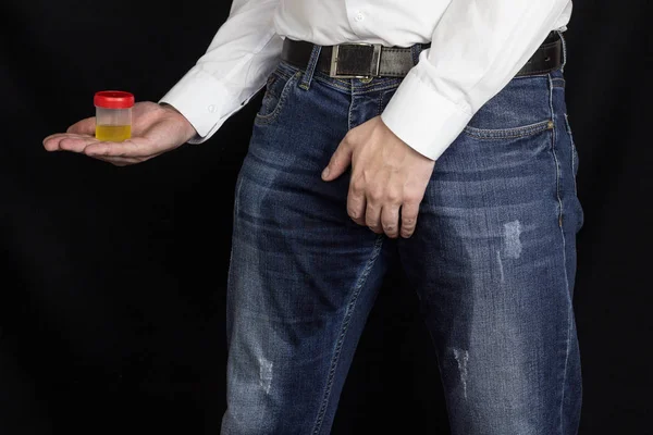 Een man houdt een monster urine in natte broek, een seks-infectie, een zwarte achtergrond — Stockfoto