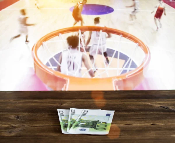 Euro geld op een houten achtergrond op de achtergrond van een Tv waarop basketbal wordt weergegeven — Stockfoto