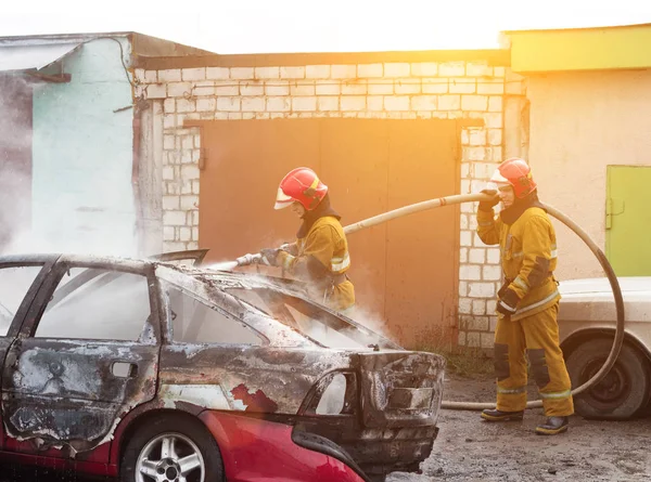 BOBRUISK, BELARUS - JULHO 25, 2018: Dois bombeiros extinguem um carro em chamas, incêndio — Fotografia de Stock