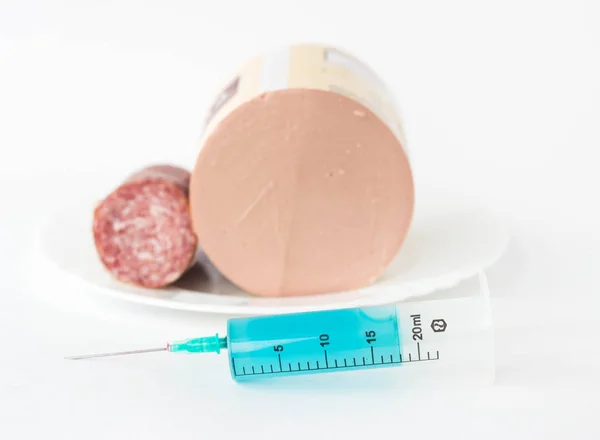 Sausage on a white background, next is a syringe with antibiotic and preservatives, close-up, snag and antibiotic