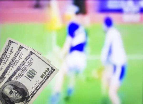 Geld Dollar auf dem Hintergrund eines Fernsehers, auf dem der Sport im Spiel von Hurling, Sportwetten, Dollar gezeigt wird — Stockfoto