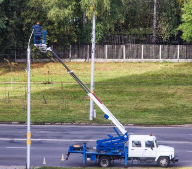 Elektrikçi elektrik direğine lambayı değiştirir, araba kulenin ampul ve iş yerine alt kutup asansörleri