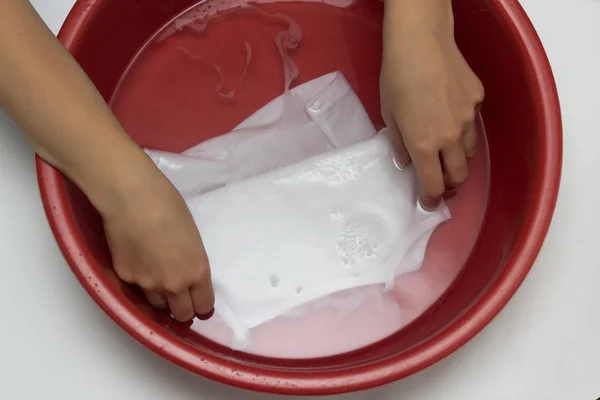 La muchacha borra la camiseta blanca infantil en el lavabo rojo de las manchas, limpia del quitamanchas, el primer plano, las manos, el fondo blanco —  Fotos de Stock
