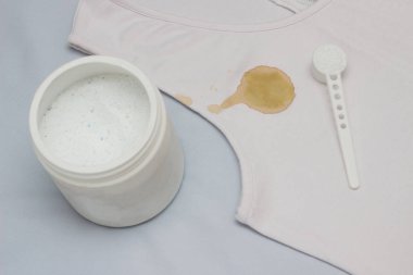 Bir kapsayıcı bir leke çıkarıcı, yakın çekim, çamaşır suyu ile beyaz bir T-shirt, yanında bir yer