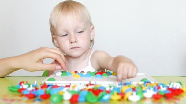 A little girl plays a game, works out a multi-colored mosaic that develops, developing motor skills and thinking in children, close-up, education, caucasian — Stock Video