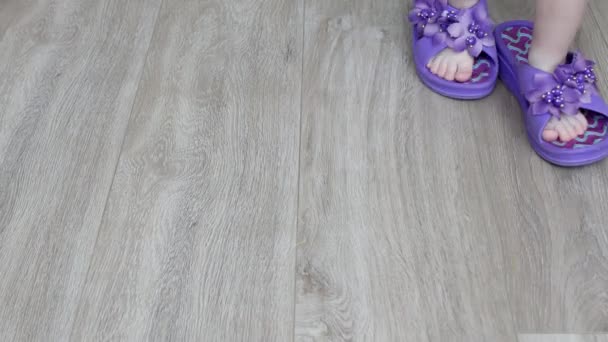 Een klein kind wandelingen in volwassen grote sneakers rond het huis, volwassen slippers op childrens voeten, home — Stockvideo