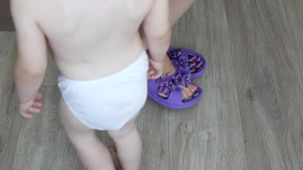 Madre toglie le scarpe da ginnastica dai piedi degli adulti, un bambino piccolo mette scarpe da ginnastica per adulti sui piedi dei bambini e cammina in loro, primo piano, a casa — Video Stock