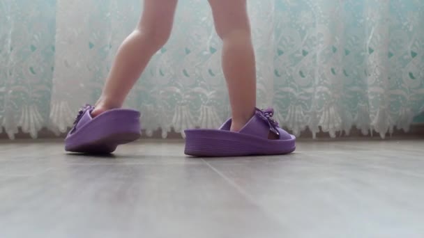 Un bambino piccolo cammina in grandi scarpe da ginnastica per adulti intorno alla casa, pantofole per adulti sui piedi dei bambini, casa — Video Stock