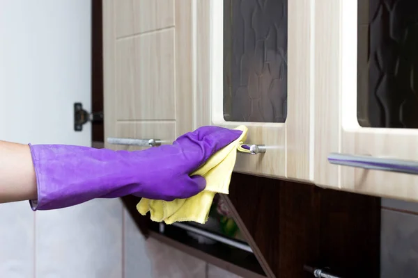 A mão feminina em uma luva roxa lava um armário de cozinha com um guardanapo e agente de limpeza, close-up, cozinha — Fotografia de Stock