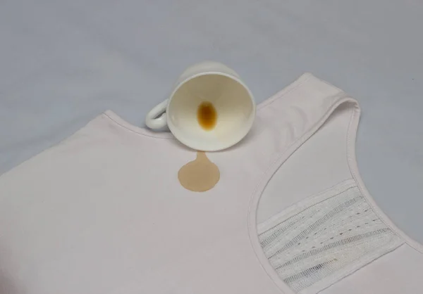 Розлита чашка кави на білій сорочці, кавова пляма на одязі, крупним планом, чашка, засіб для видалення плям — стокове фото
