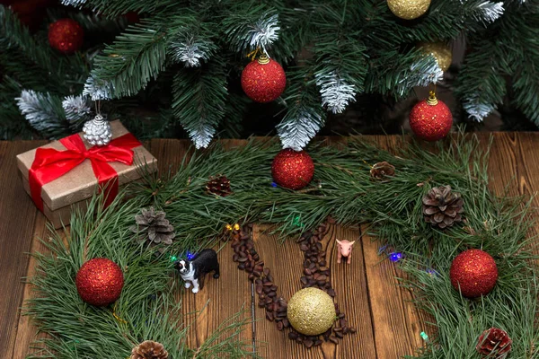 Новогодние часы из елки и новогодних игрушек, коробка с новогодним подарком, игрушечные свиньи и собаки, на фоне новогодней елки, деревянный фон — стоковое фото