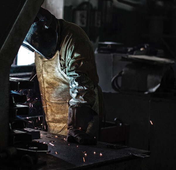 Welder at the factory welds metal parts, welding and sparks, dirty production, harmfulness, brickwork