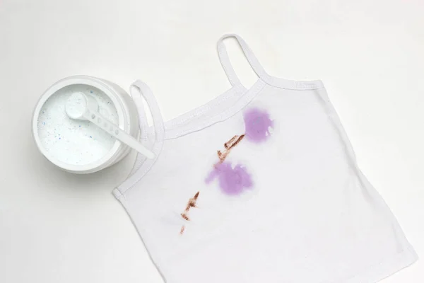 Children's white T-shirt with spots, next to the container with stain remover, close-up, white background — Stock Photo, Image