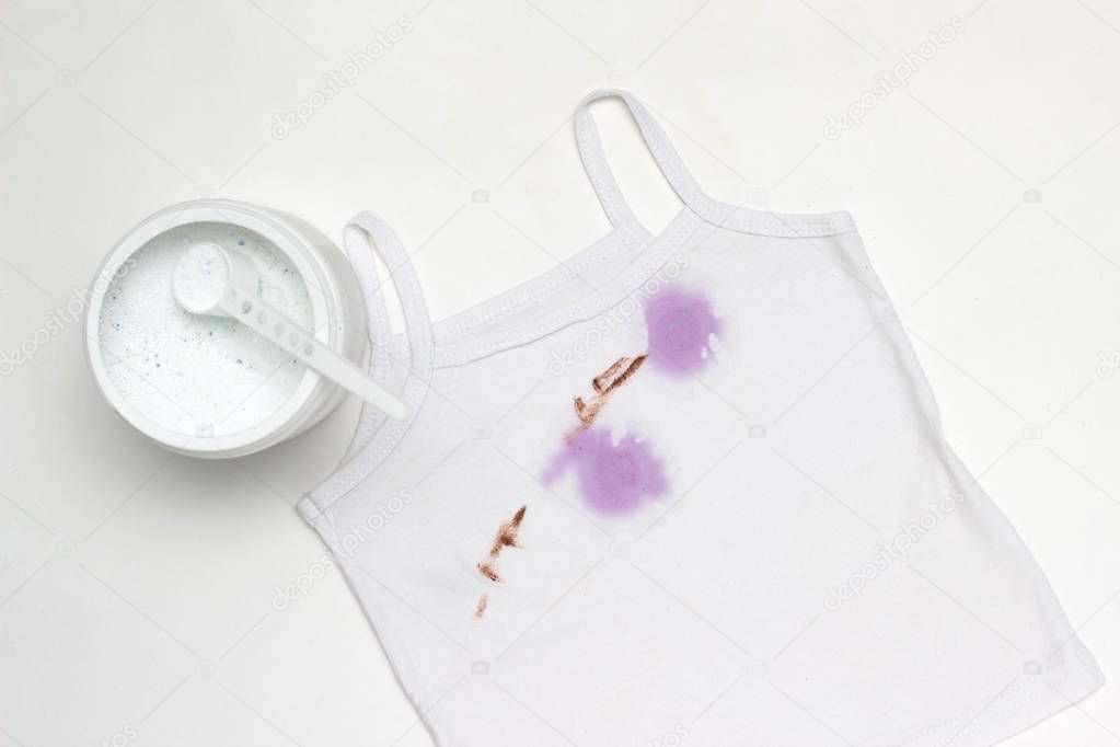 Children's white T-shirt with spots, next to the container with stain remover, close-up, white background