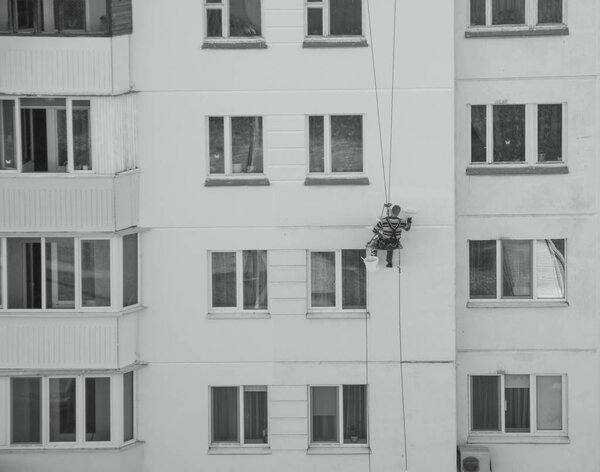 A worker climber paints a residential high-rise building and seals up joints in a house, painting a residential house, toned