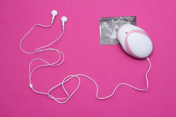 妊娠中の女性や妊娠、クローズ アップ、ピンクの背景の超音波の画像で赤ちゃん s 心臓の鼓動を聴くためのヘッドフォンで胎児ドップラー — ストック写真