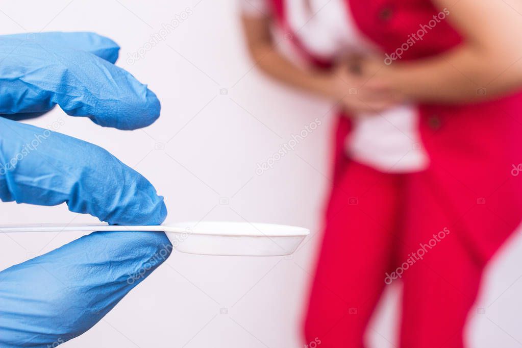 Doctor in a medical glove holding a spoon with medicine in the background a girl holding her stomach, stomach pain, gastritis, close-up