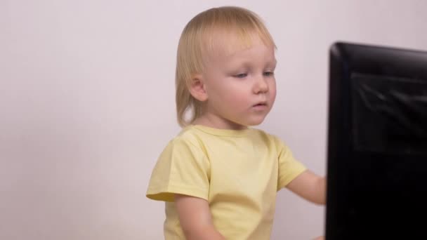 Lilla kaukasiska flicka blonda ser in dator laptop skrattar och grimaser, närbild, känslor — Stockvideo