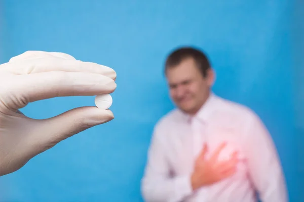 Ein Arzt in einem medizinischen Handschuh, der eine Pille gegen Herz-Kreislauf-Erkrankungen in der Hand hält, ein männlicher Patient, der sein Herz hält, Herzprobleme, medizinische — Stockfoto