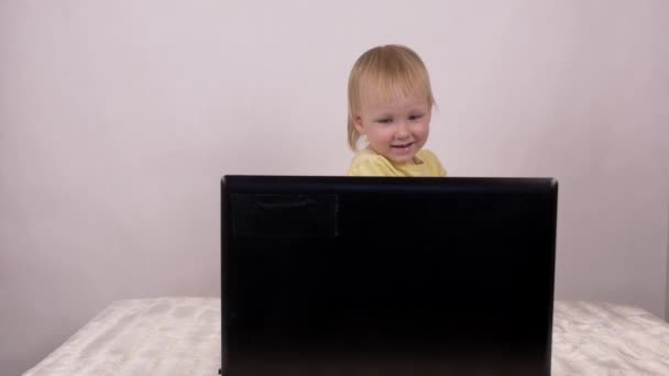 Piccola ragazza caucasica bionda guarda nel computer portatile ride e smorfie, primo piano, emozioni — Video Stock