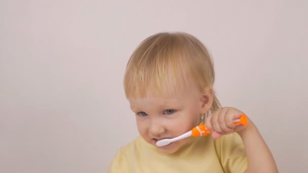 Menina caucasiana limpa os dentes em um fundo branco, câmera lenta, escova de dentes — Vídeo de Stock