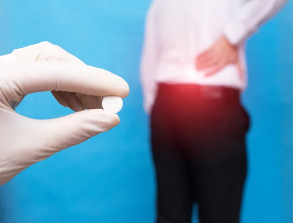 The doctor holds a pill for back pain, in the background is a man who has a backache, an intervertebral hernia and osteochondrosis, sciatica, anti-inflammatory drugs