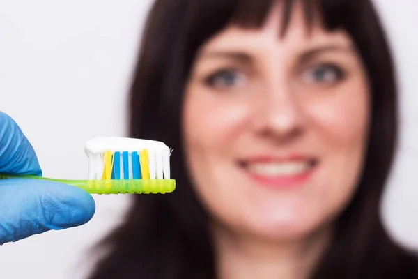 Doctor holding a toothbrush with a toothpaste in the background smiling caucasian girl with a smile, medical, close-up — Stock Photo, Image