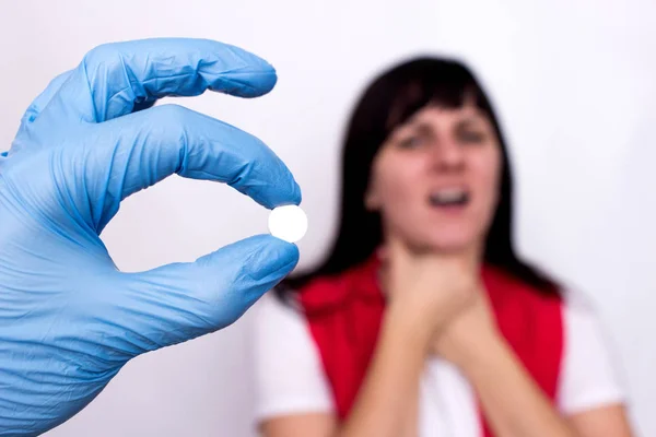 El médico sostiene una píldora antiséptica en su mano para una enfermedad de la garganta, en el fondo una chica cuyo dolor de garganta tiene dolor de garganta, una cura para enfermedades de la garganta, inflamación — Foto de Stock