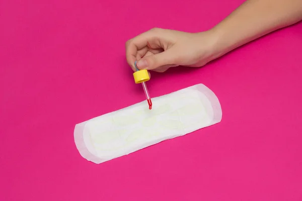 Une main féminine tient une pipette dans sa main et goutte du sang sur une serviette hygiénique, concept de menstruation, fond rose, espace de copie, intime, pms — Photo