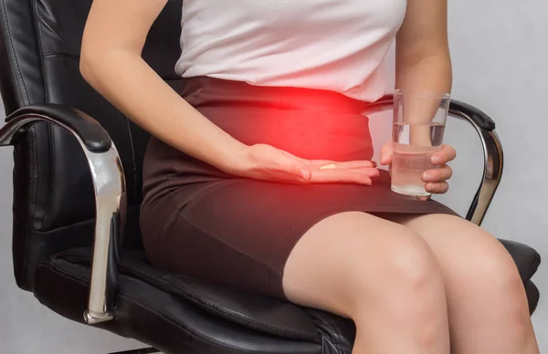 Девушка сидит в офисном кресле и держит таблетку от боли во время менструации, бизнеса, крупного плана, противовоспалительного — стоковое фото
