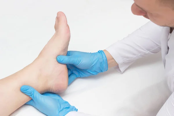 Médico examina a perna do paciente com esporas de calcanhar, dor no pé, fundo branco, close-up, fascite plantar — Fotografia de Stock