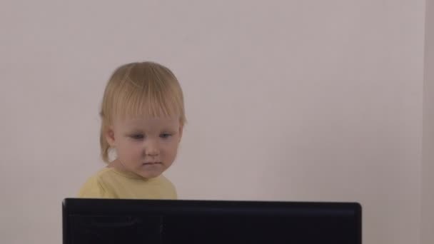 En liten flicka spelar och leker med en bärbar dator, visar olika känslor på hennes ansikte, långsamma-mo — Stockvideo