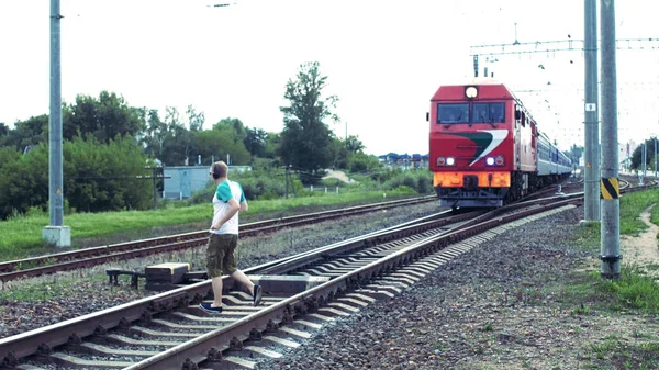 Un homme caucasien en casque écoute de la musique et traverse le chemin de fer juste sous le train, danger sur le chemin de fer — Photo